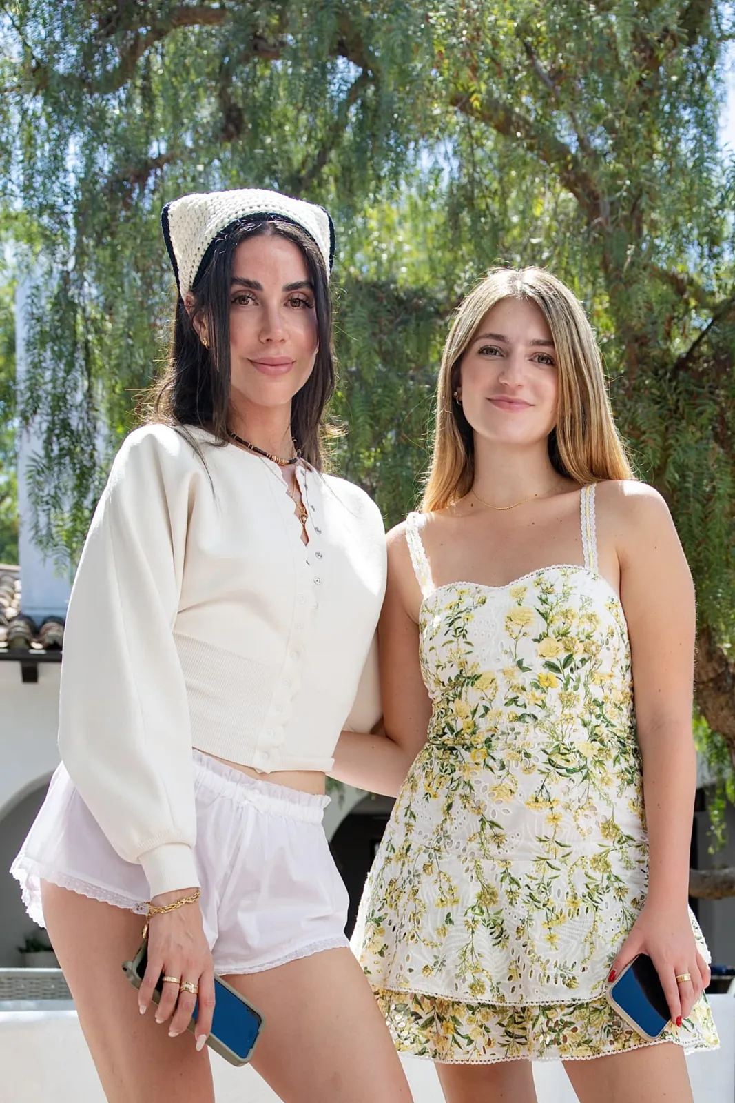 Two women in summer whites and florals beneath a pepper tree