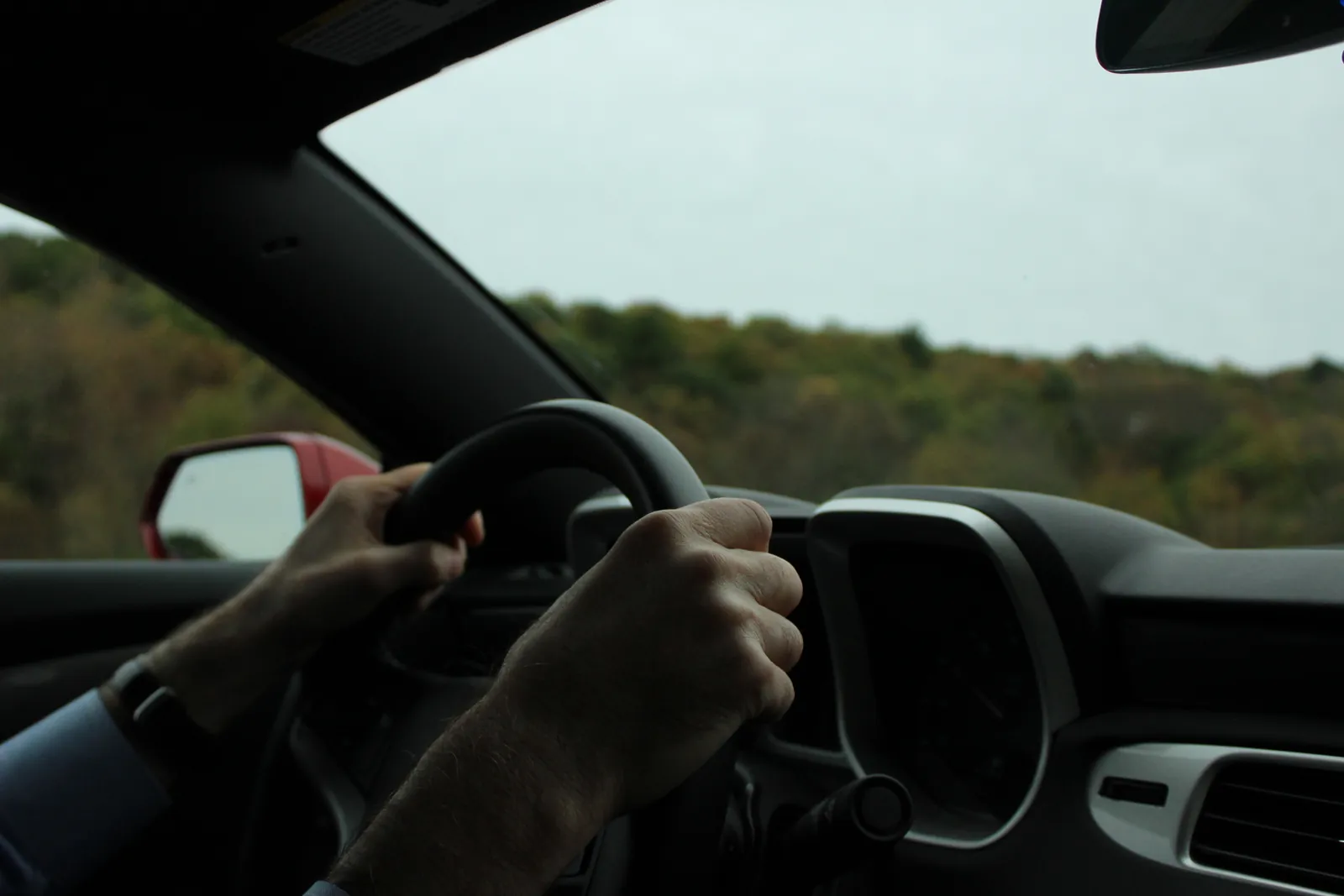 Hands on a steering wheel on an overcast autumn road trip