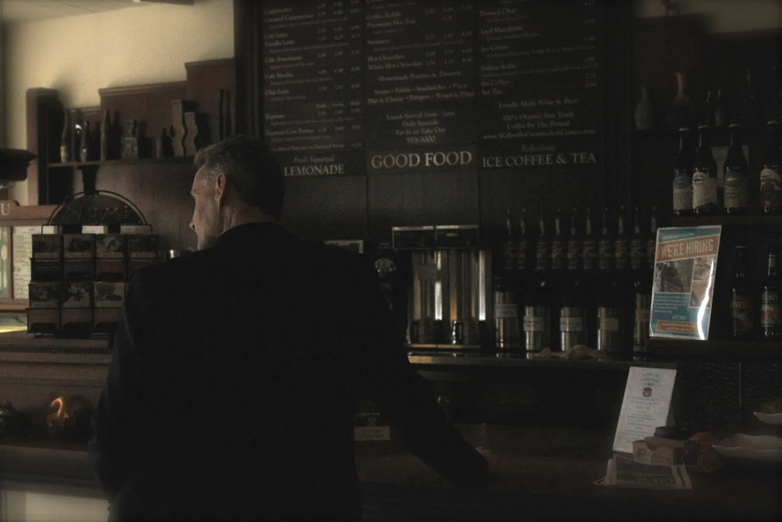 Cinematic warm-toned scene of a man at a coffee shop counter