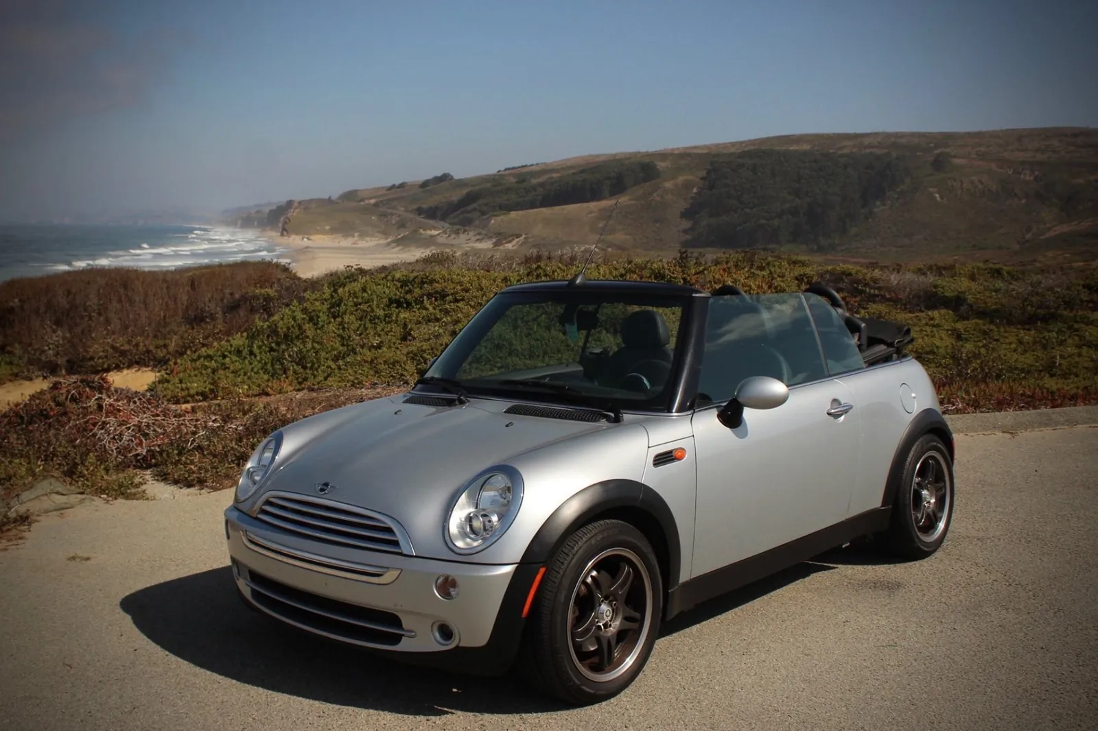 Silver Mini convertible parked beside a coastal highway