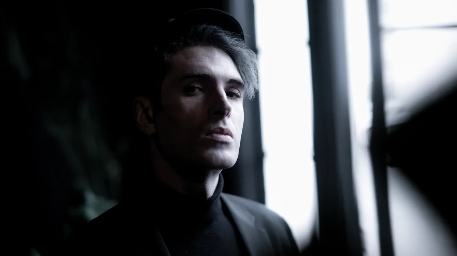 Moody window-light portrait of a man in dark tailored clothing